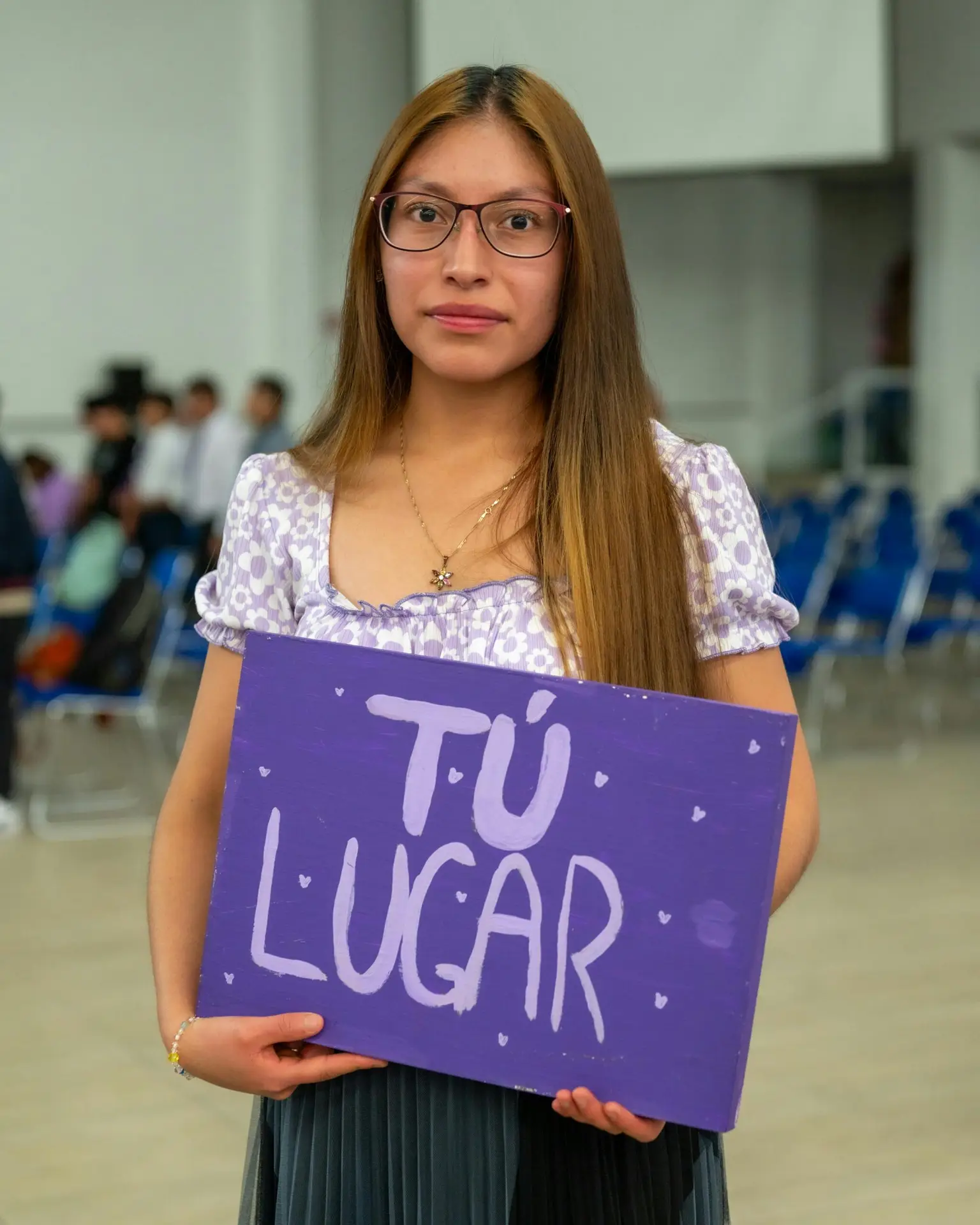 A young woman inside an auditorium holding a sign with 'Tú Lugar' written on it.